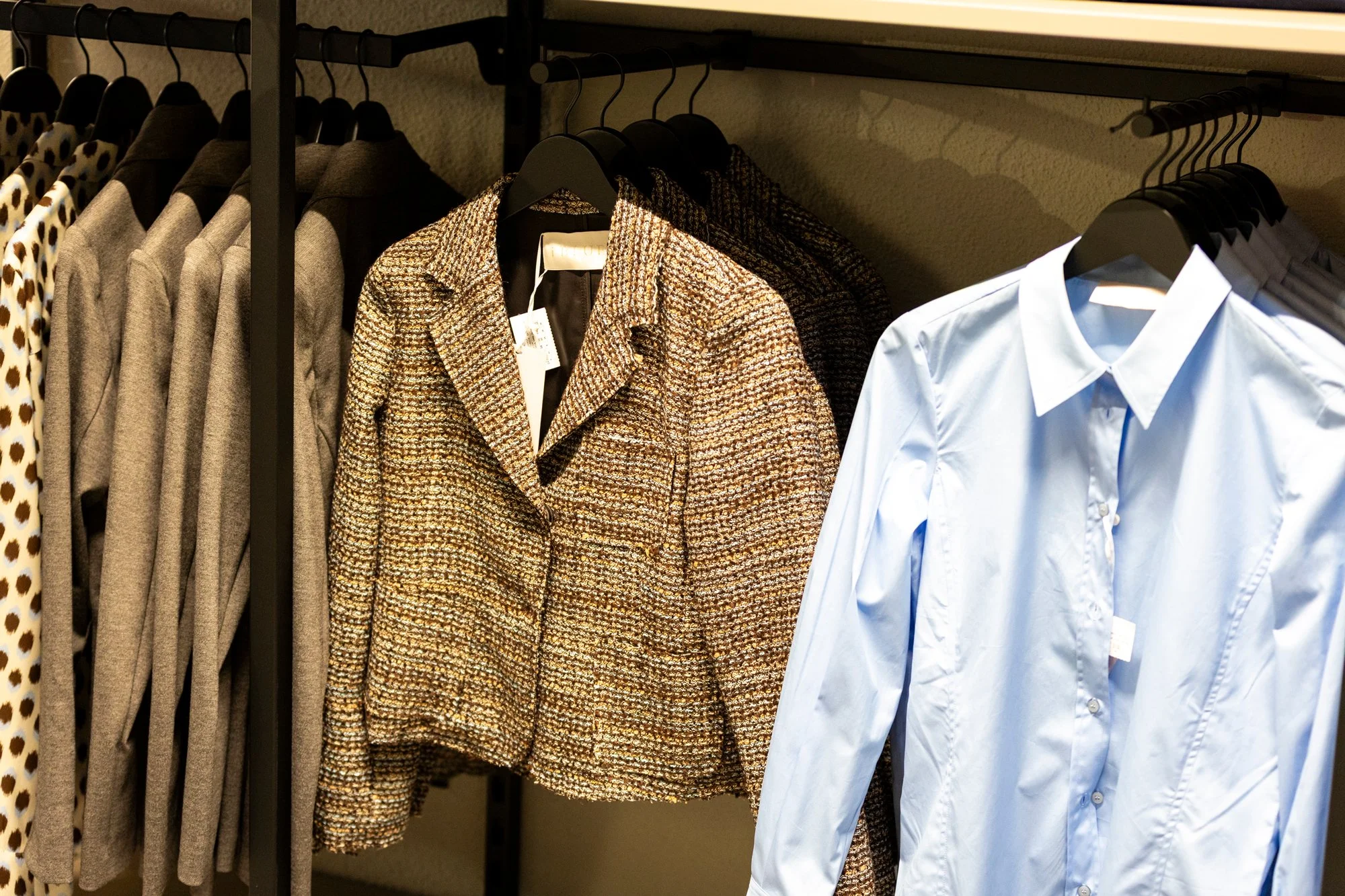 Herrenmode in einem Bekleidungsgeschäft, inklusive Kostümjacken, Blusen und Hemden an Kleiderbügel.