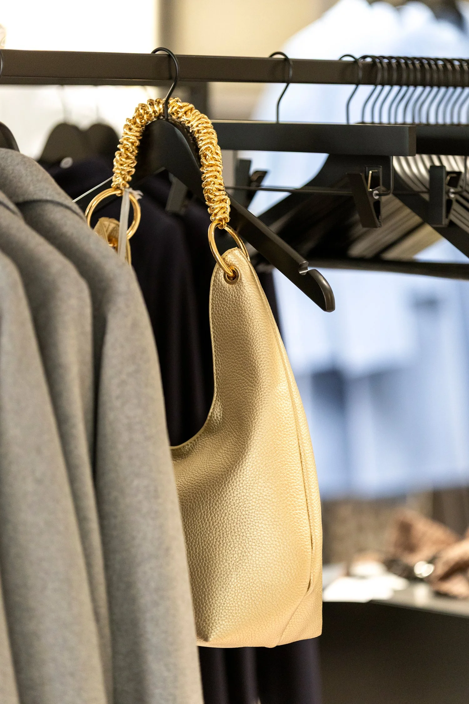 Nahaufnahme von Designer-Handtasche mit goldenen Kettenhenkeln, im Einzelhandel auf Kleiderbügel an Kleidung.