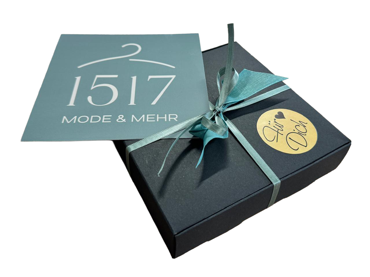 Schwarze Geschenkbox mit silbernem Band, darauf ein Aufkleber mit der Aufschrift 'Für Dich' und ein blauer Zettel mit der Aufschrift '1517 Mode & Mehr'.