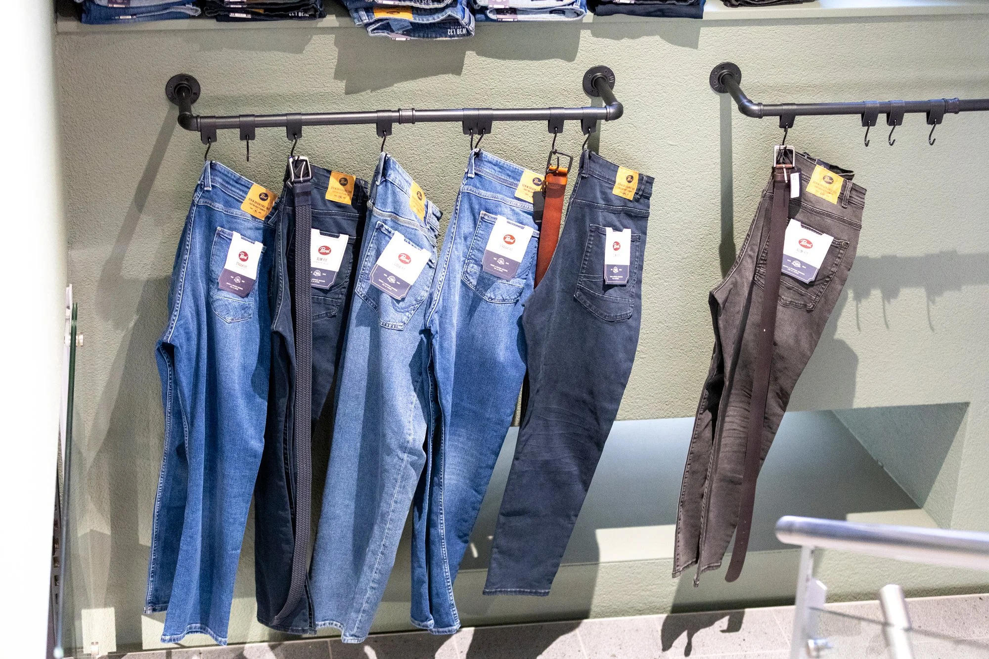 Jeans und Hosen hängen an einer schwarzen Garderobe im Bekleidungsgeschäft.