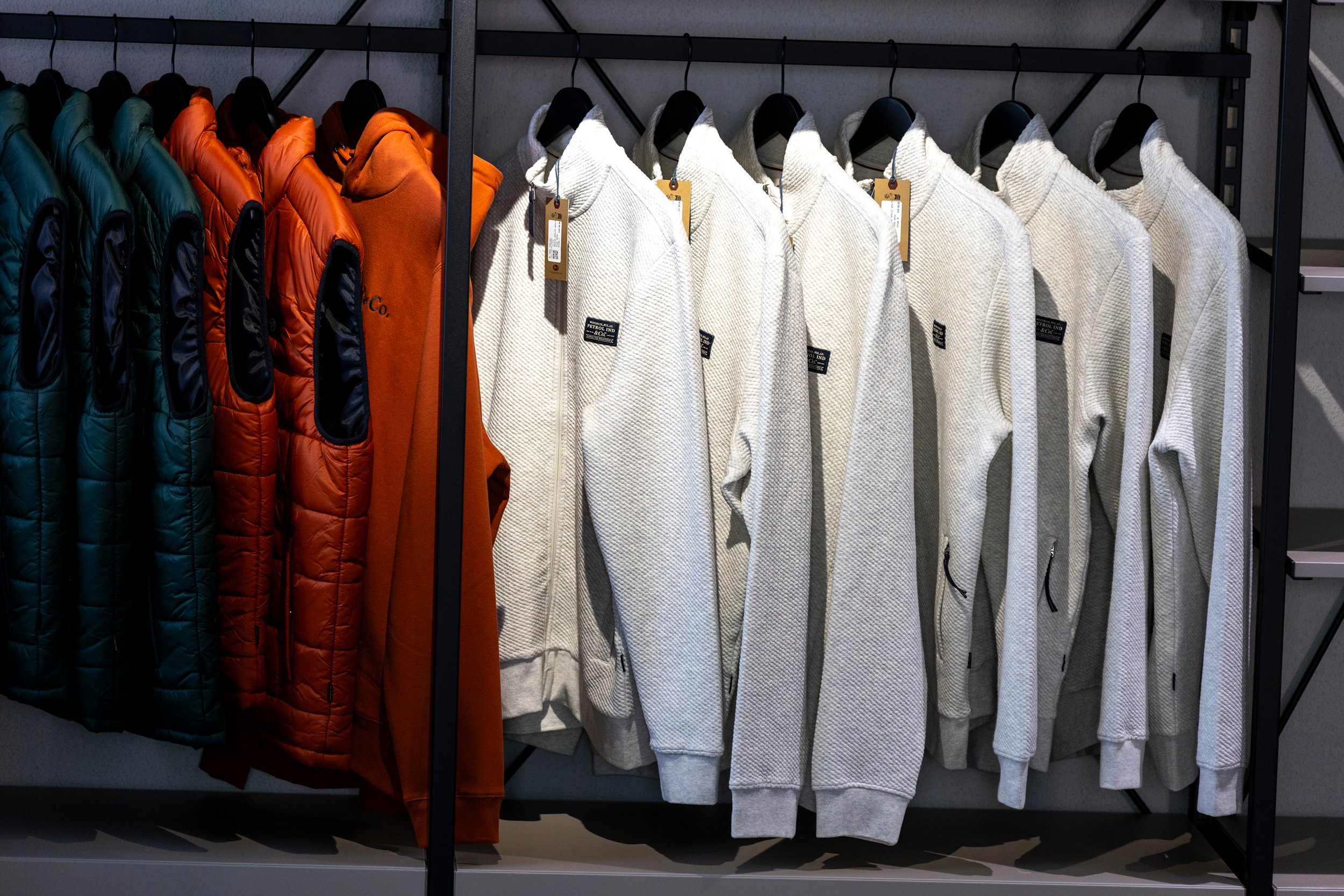 Verschiedene Oberbekleidung, darunter Farben und Pullover, hängen an einem Metallkleiderständer in einem Geschäft.