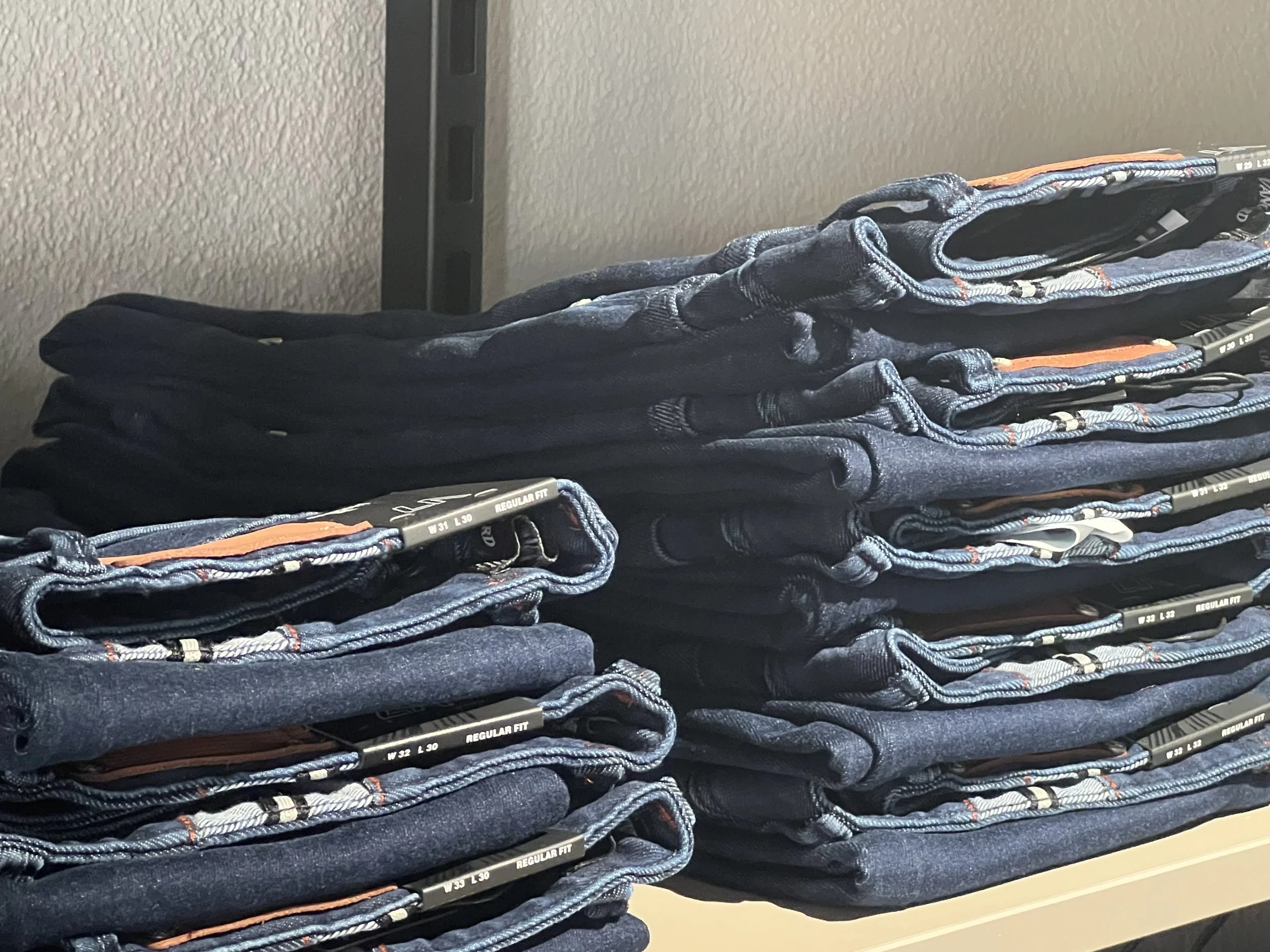 Haufen gefalteter Jeans auf einer Verkaufsregal-Ebene.