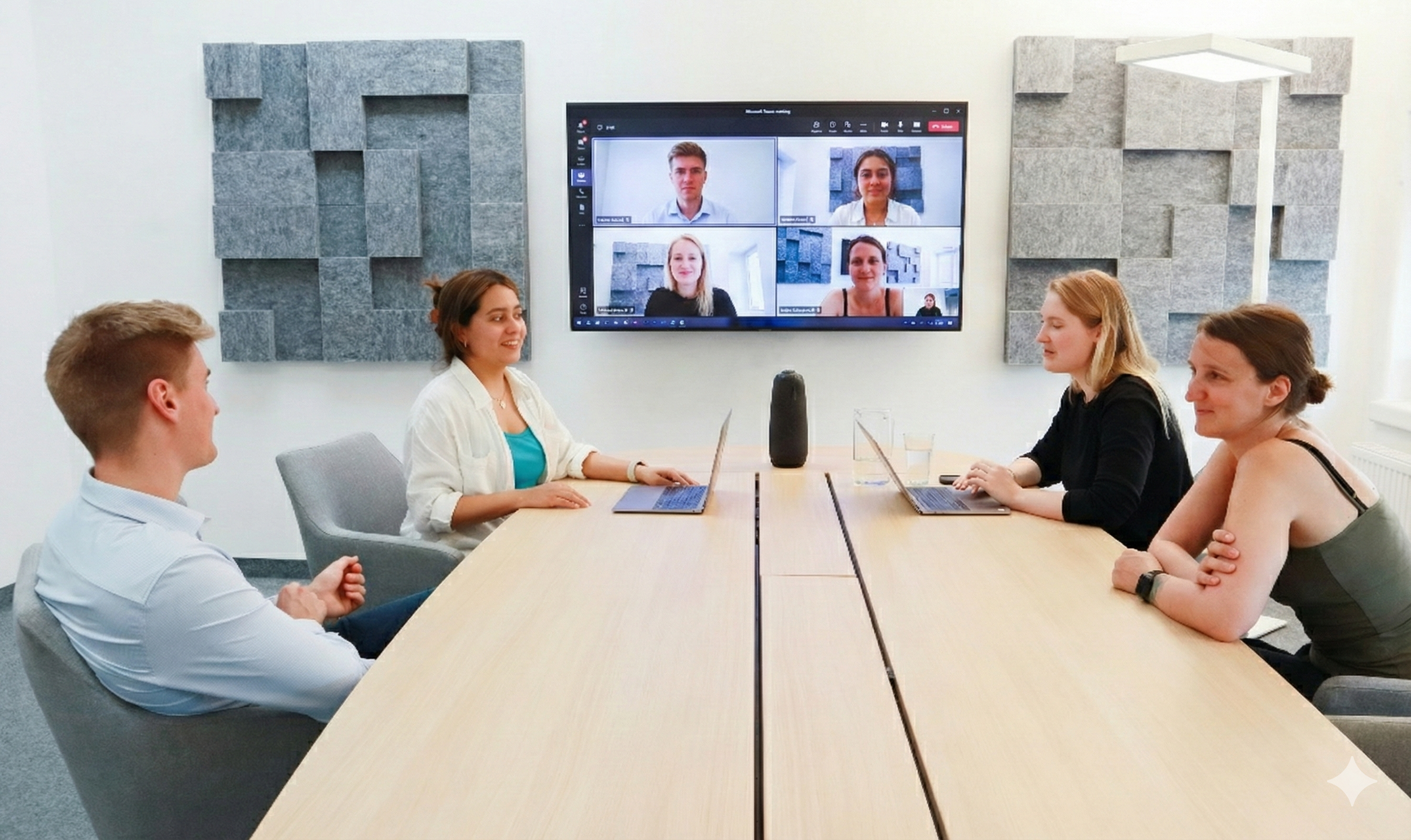Vijf mensen zitten rond een konferentietafel in een vergaderkamer met een groot scherm waarop een videoconferentie te zien is. Administratieve jobs, bureau.