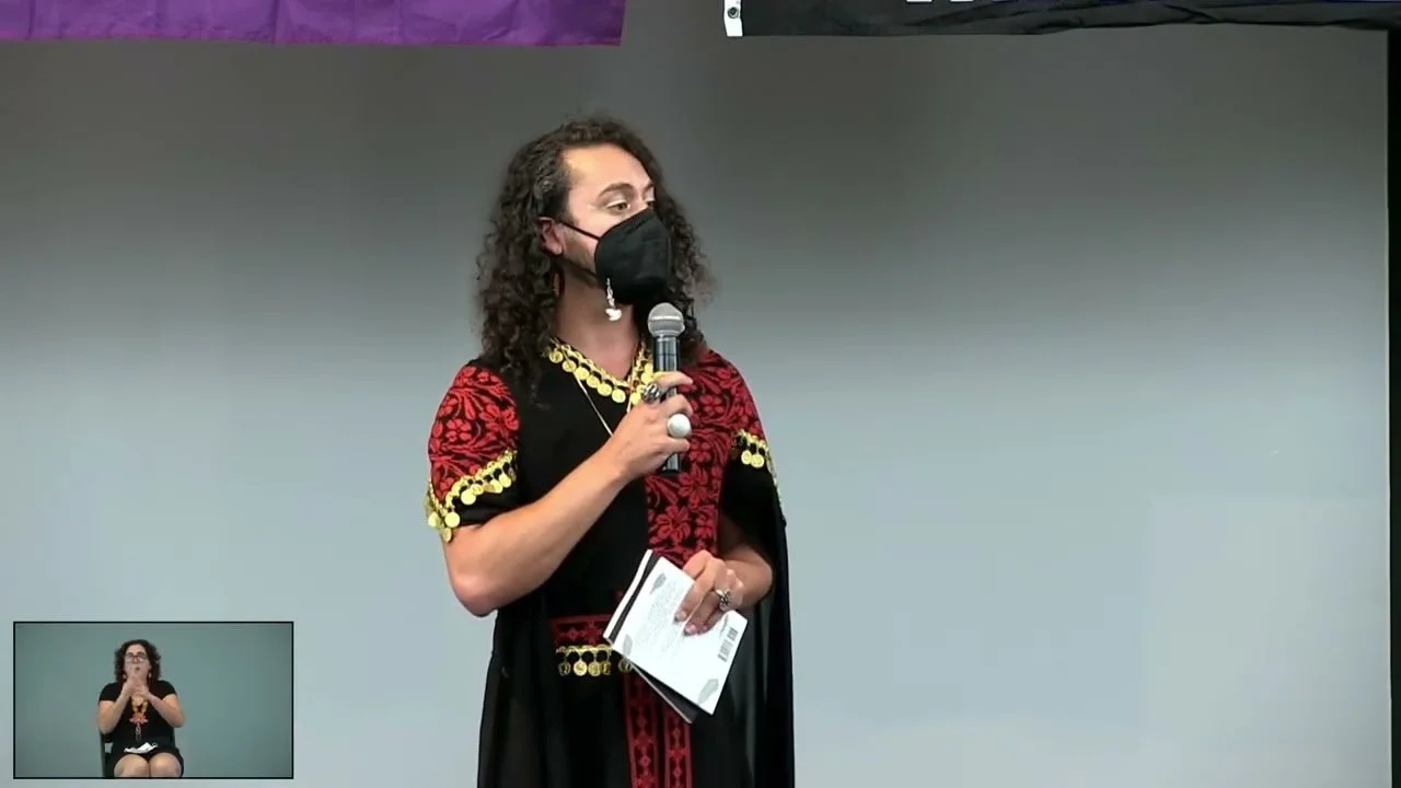 Thumbnail of "Decolonized Beatz Indigenous World Pride 2025 - Day 01 - Yaffa"

Wearing a black face mask, Yaffa is holding a microphone and a book.