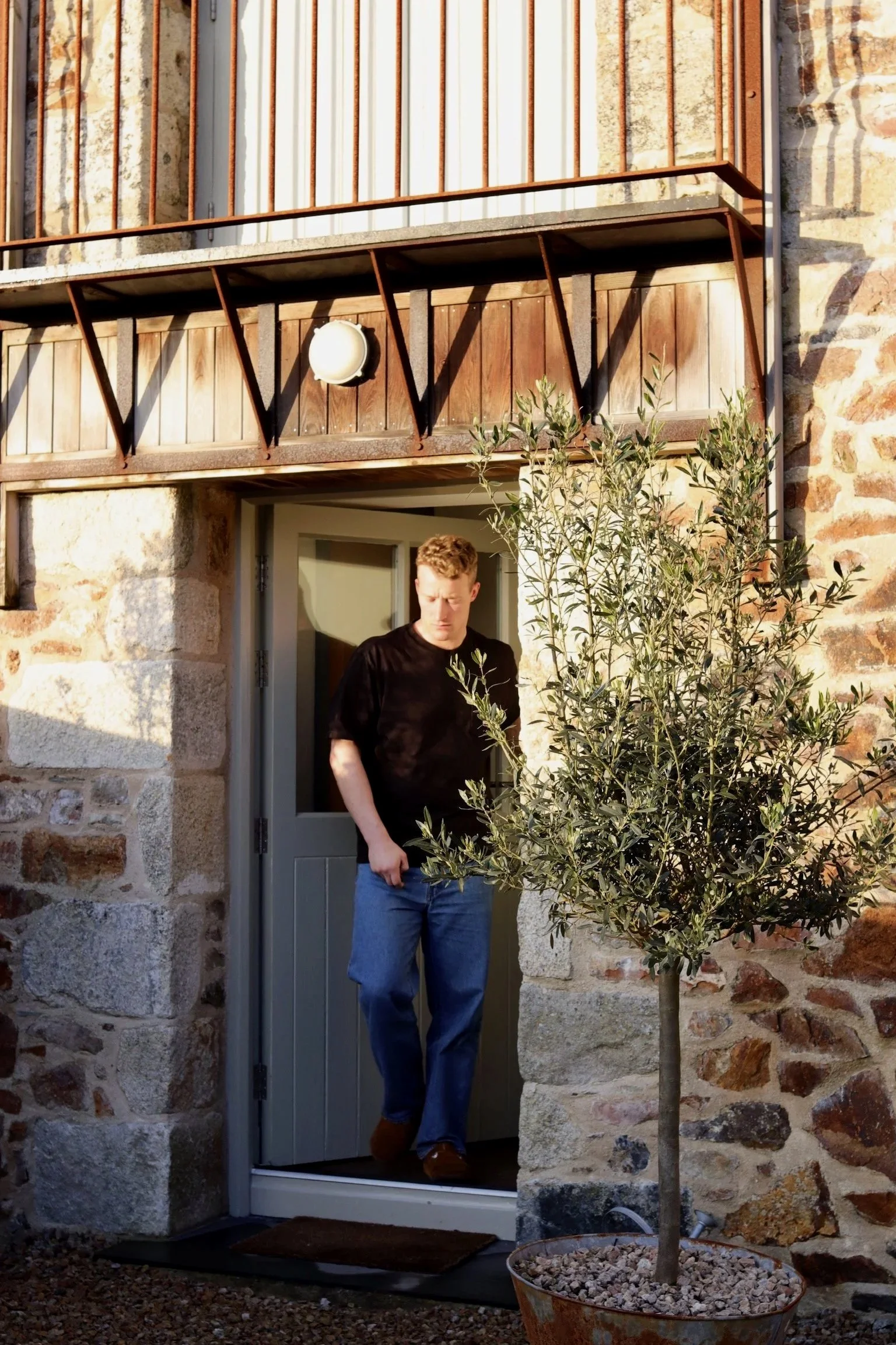 Stone entrance to Stargazey barn with wooden balcony and coastal planting.