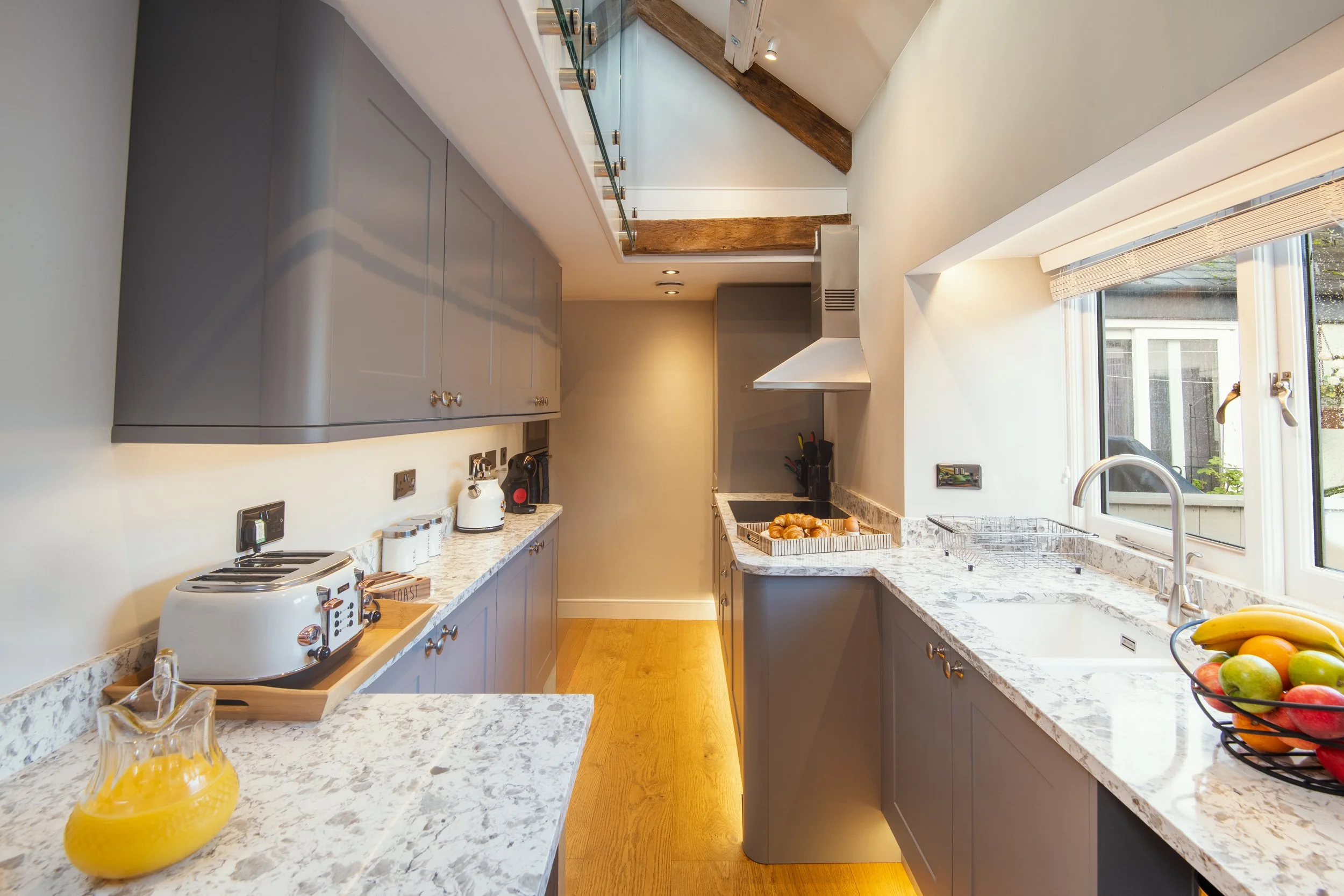 A modern kitchen with blue cabinets, marble countertops, and stainless steel appliances, including a toaster and a sink with a view outside through a window.
