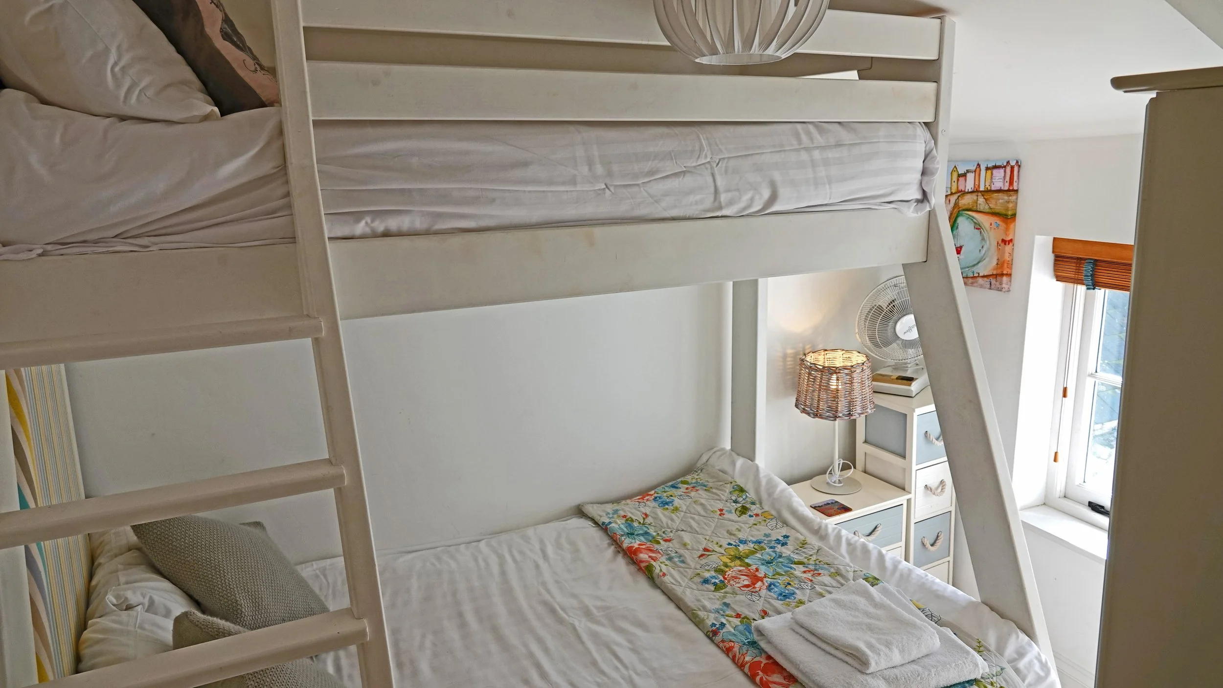 Bedroom with white bunk beds, a nightstand, a lamp, and a window with a curtain.
