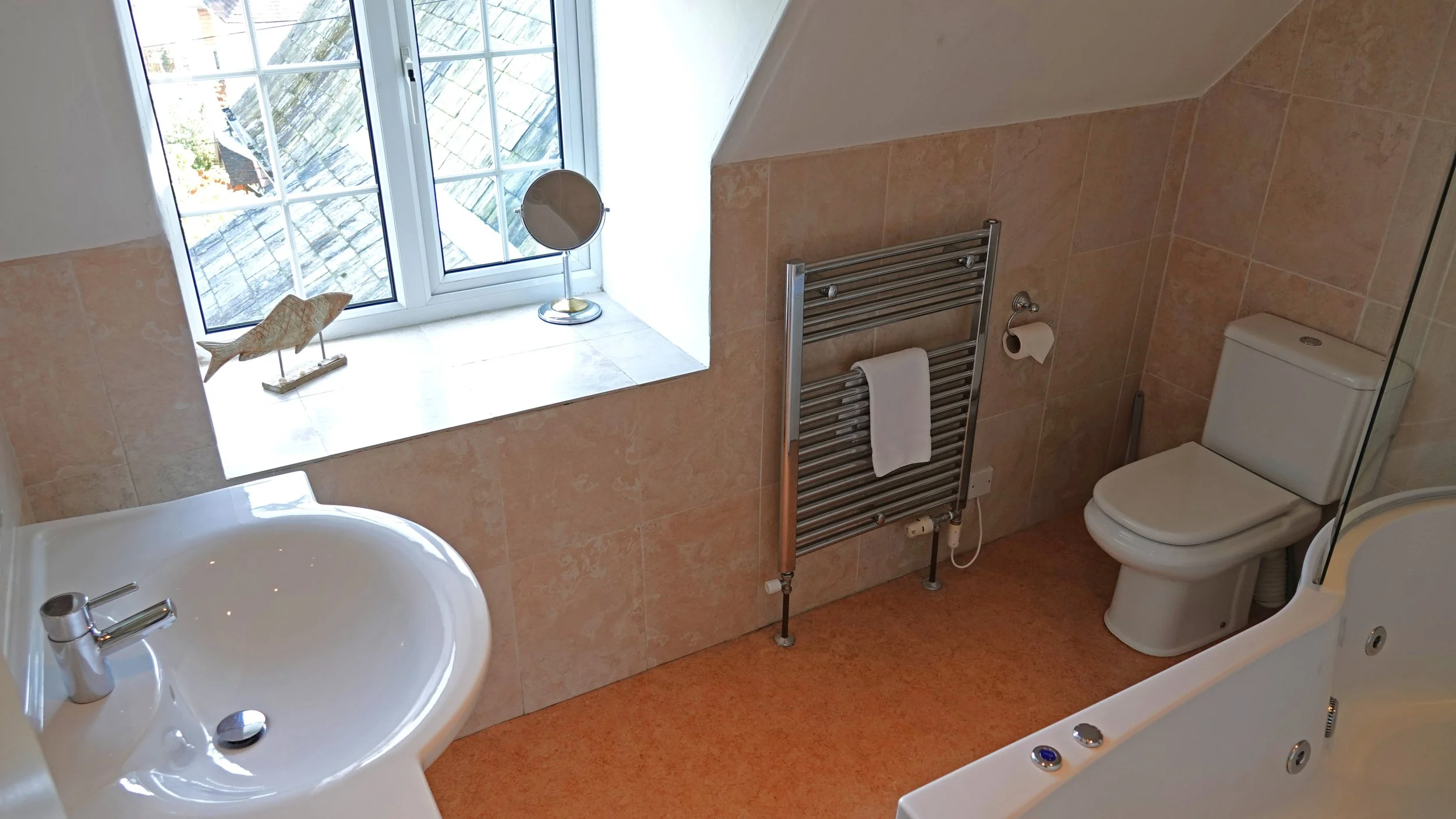 Bathroom with a window, sink, toilet, heated towel rail with towel, and a bathtub with jets.