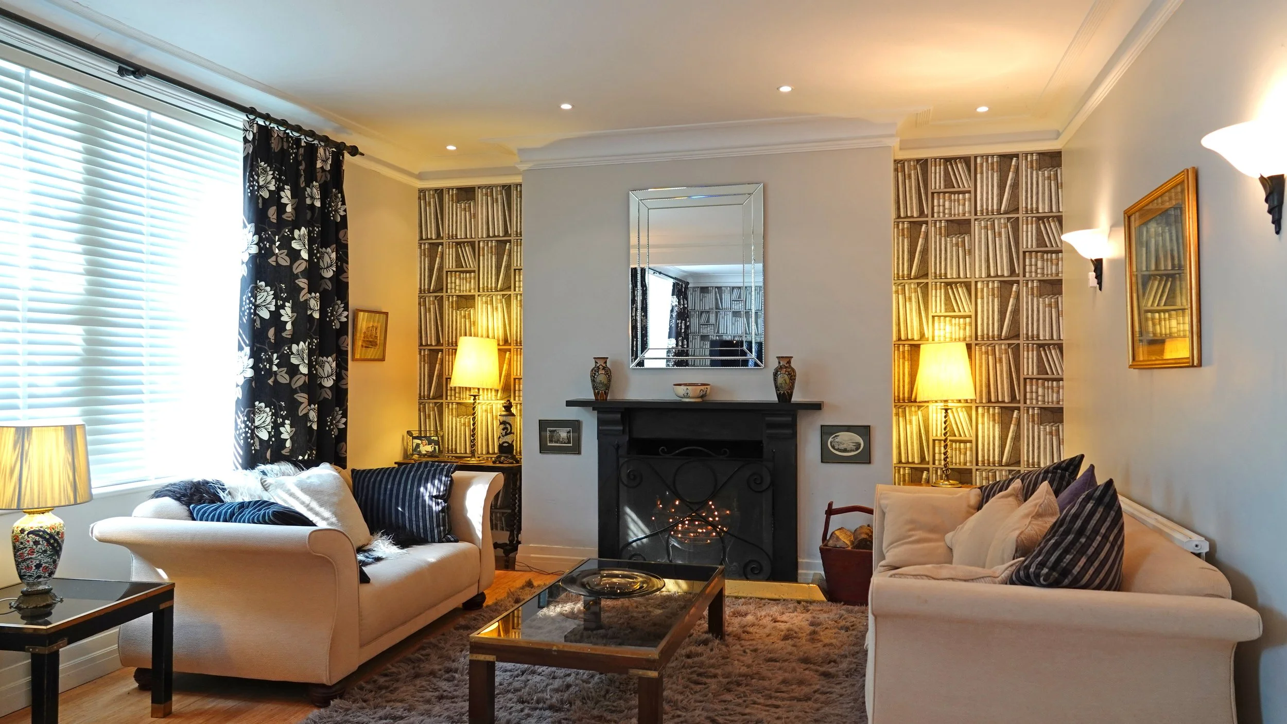 Living room with beige sofas, a black fireplace, bookshelves, and warm lighting.
