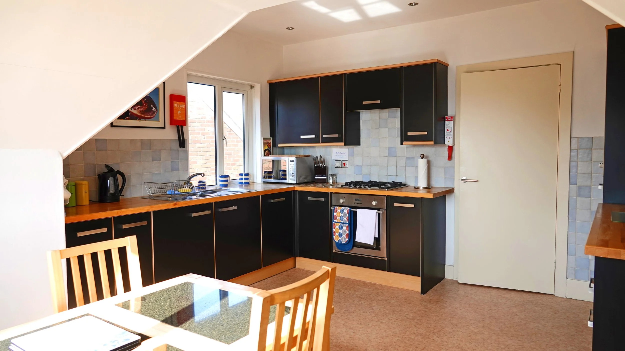 Kitchen with black cabinets, a wooden countertop, a gas stove, microwave, paper towel roll, and a window near the sink, with a table and chairs in the foreground.