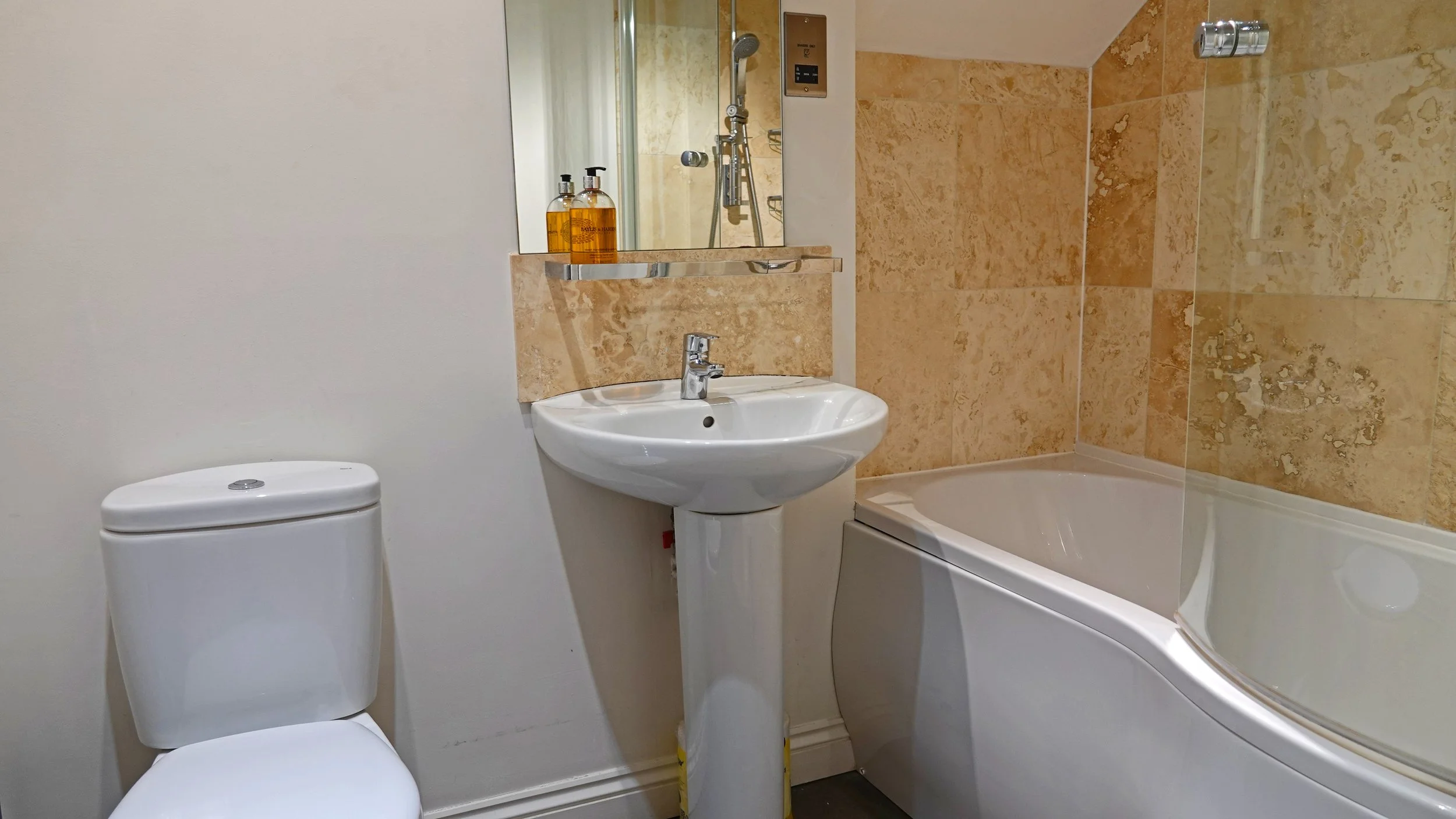 Bathroom with toilet, small sink, and bathtub with beige marble tiles.