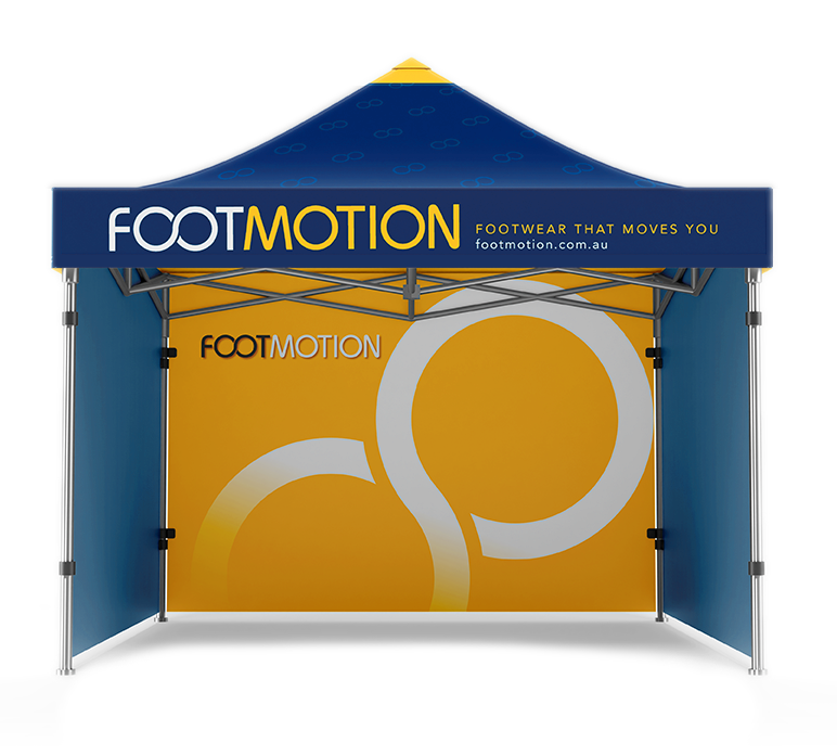 A promotional booth for FootMotion, a footwear company, featuring a blue canopy with yellow text and a large yellow backdrop with white circles and the FootMotion logo.