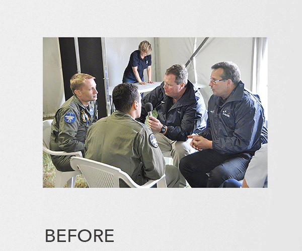 Four men, two in military uniforms and two in casual jackets, sitting in a semi-circle having a discussion with one man holding a microphone. A woman is in the background writing on a clipboard.