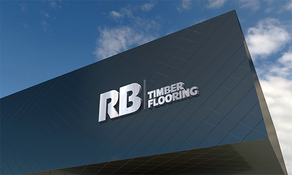 Close-up of a building's exterior with a large logo reading 'RB Timber Flooring' on a dark, tiled facade against a partly cloudy sky.