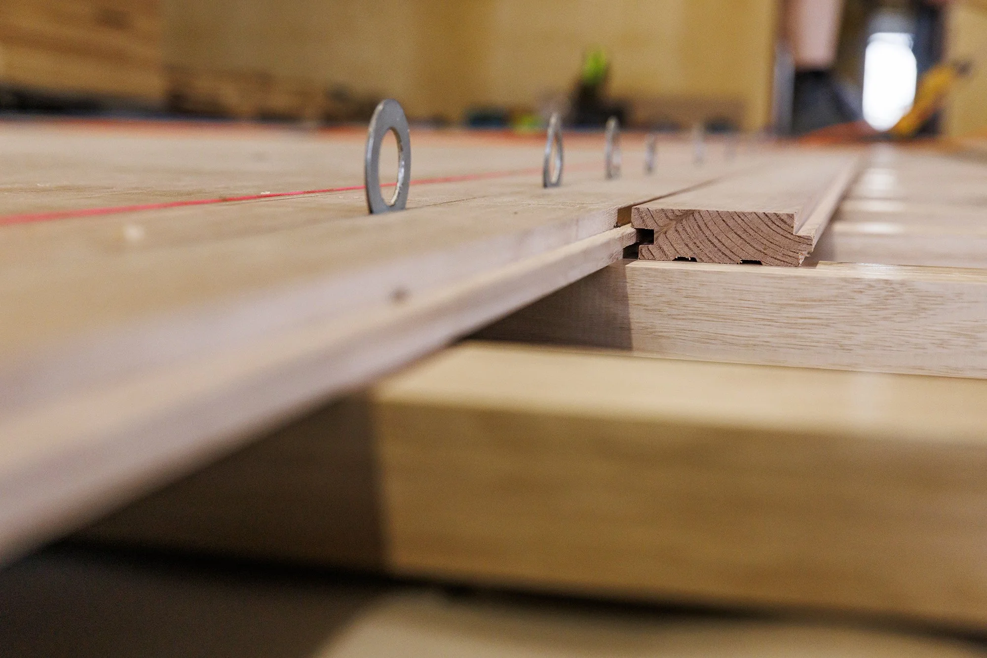 Close-up of a woodworking project showing a piece of wood with metal washers placed along a red string, possibly for alignment or measurement on a worktable in a workshop.