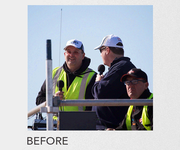 Three men in safety vests and caps speaking into microphones on a platform outdoors.