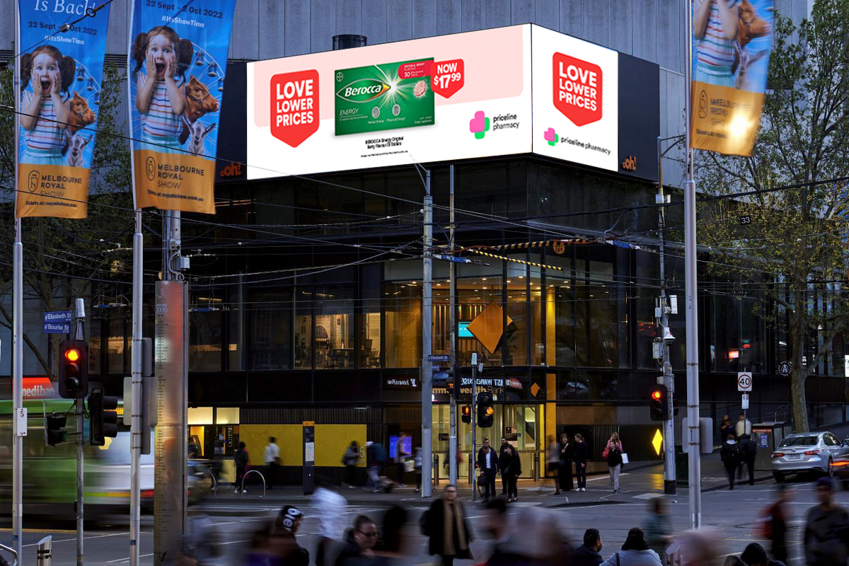 A busy city street scene at dusk with pedestrians crossing the street, a Green and white Berocca billboard advertising a price reduction, and yellow Melbourne Royal Show banners with children on display. The building features large glass windows showing an interior with bright lighting.