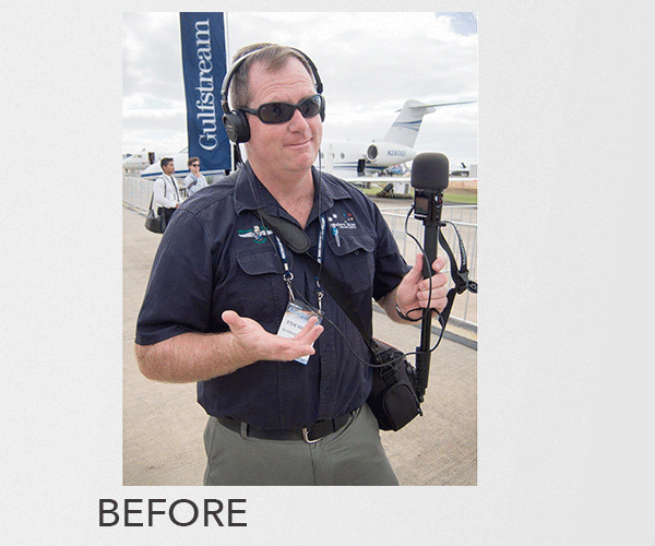 A man wearing sunglasses, headphones, and a dark shirt with a logos, standing outdoors at an airport with small aircrafts in the background, holding a microphone and a recording device.