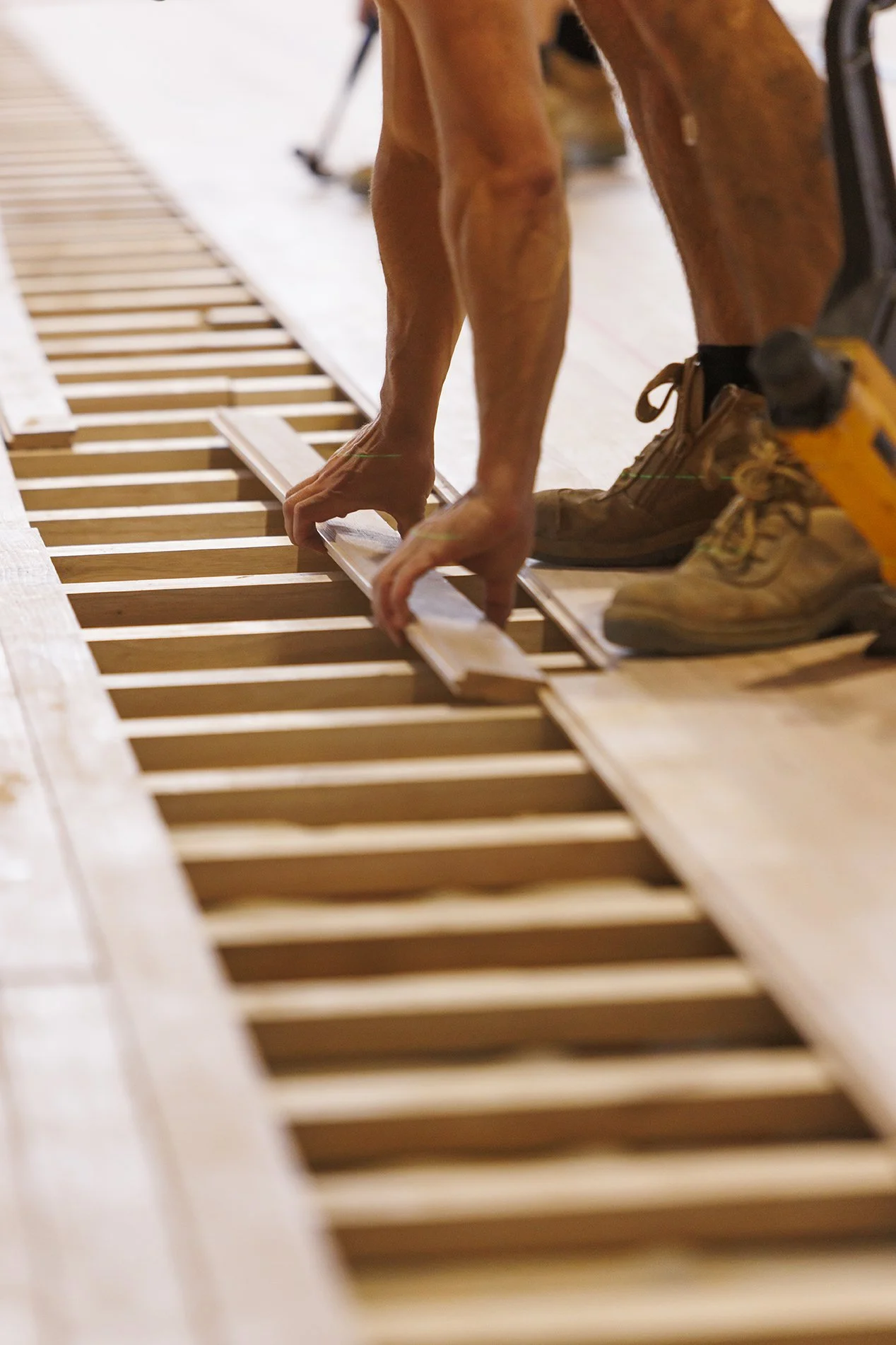 Close-up of a person installing wooden flooring with their hands, surrounded by wooden planks, using tools to fit the boards together.