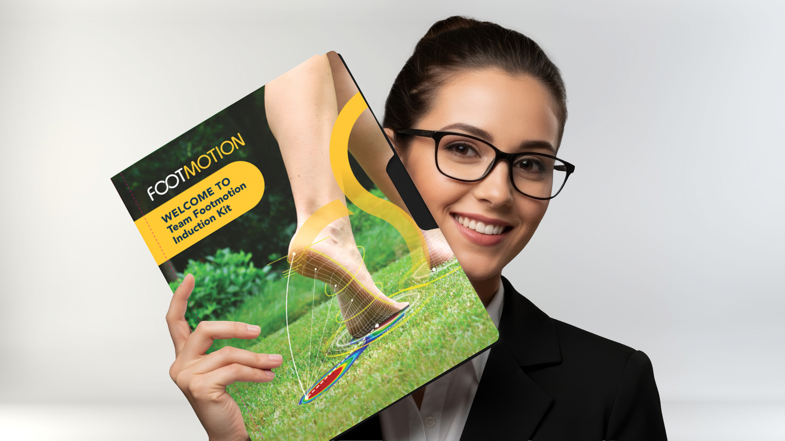 A woman with glasses and a black blazer holding a colorful booklet titled "Footmotion: Welcome to Team Footmotion Induction Kit" in front of a plain white background.