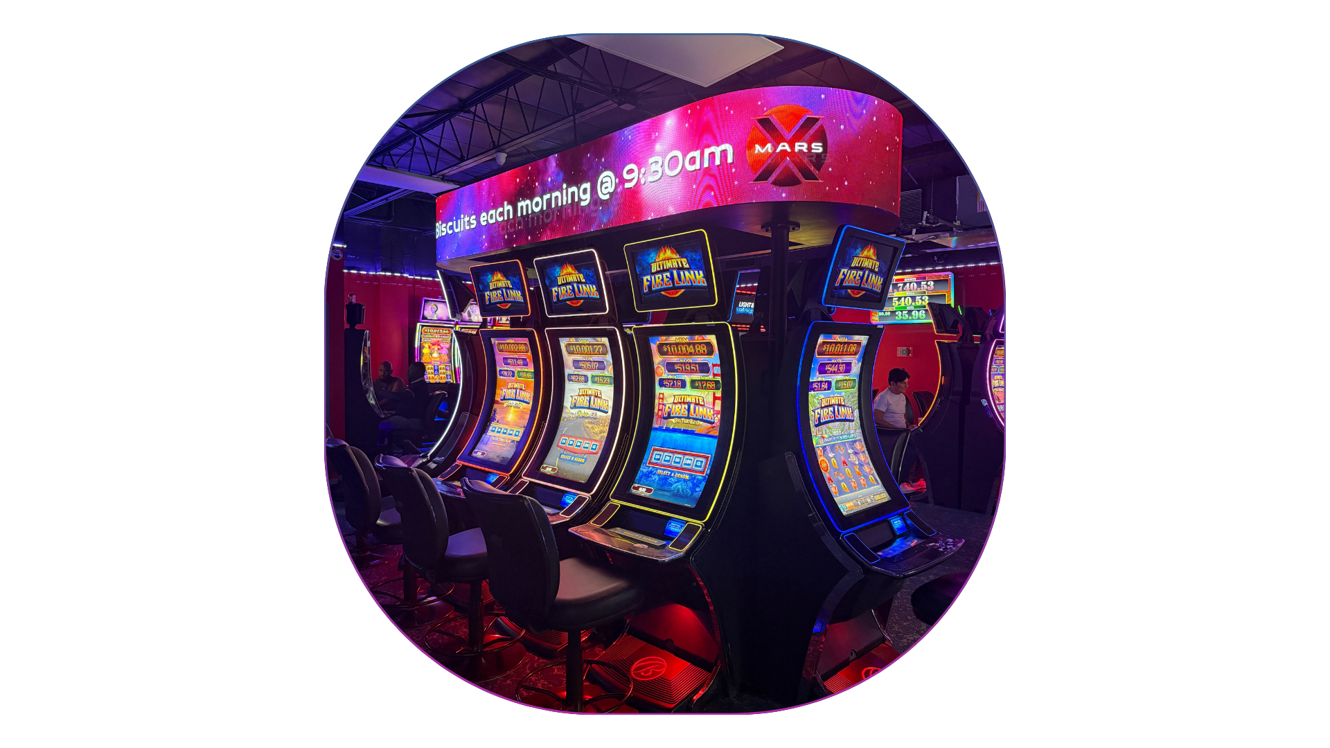Arcade gaming area with multiple slot machines and chairs, illuminated by colorful neon lights, inside a gaming arcade or entertainment center.