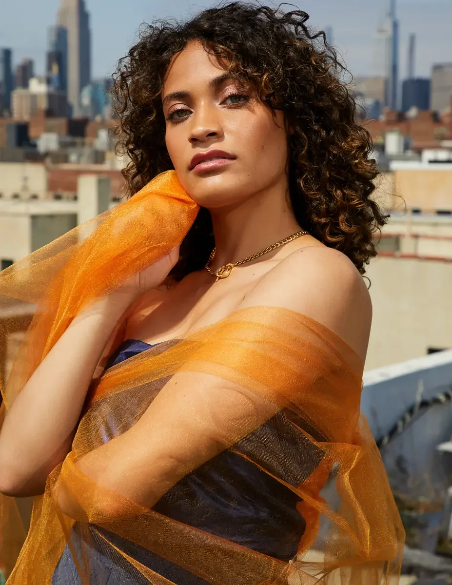 Fashion test shoot, close portrait of model Ireland T in Amy Page DeBlasio navy strapless top, orange tulle wrapped at shoulder, Manhattan skyline, East Village rooftop, New York City, styling by Matsine Stinson, makeup by Stefani Paige Vivian, photo