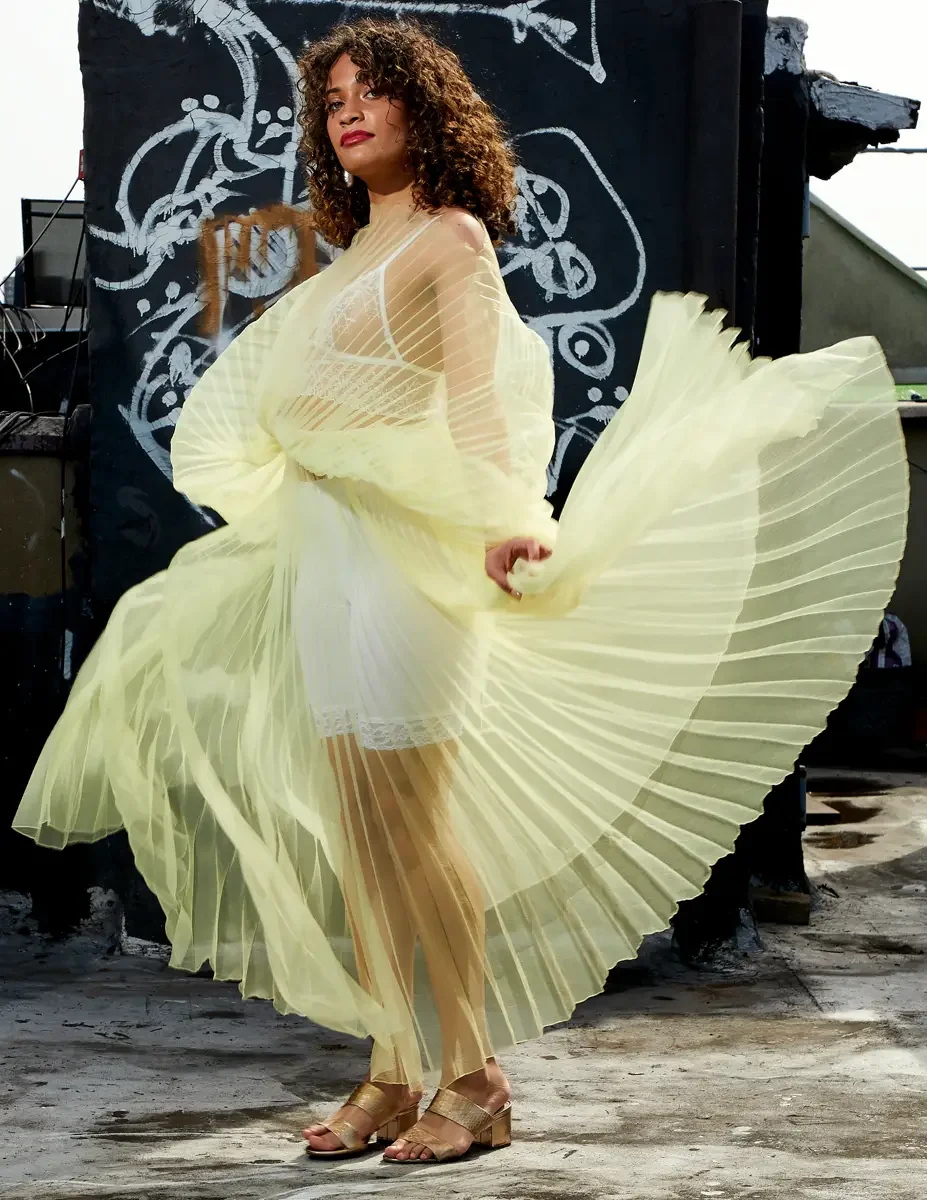 Fashion test shoot, model Ireland T in J'Amemme yellow pleated sheer gown, skirt sweeping wide, graffiti wall backdrop, East Village rooftop, New York City, styling by Matsine Stinson, makeup by Stefani Paige Vivian, photographed by Scott Parker Phot