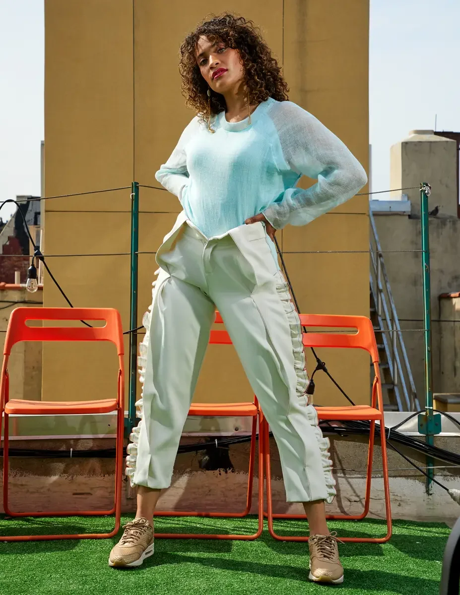 Fashion test shoot, full-length, model Ireland T in Amy Page DeBlasio white ruffle-trim pants and aqua sheer knit top, ruffle seam detail visible, East Village rooftop, New York City, styling by Matsine Stinson, makeup by Stefani Paige Vivian, photog