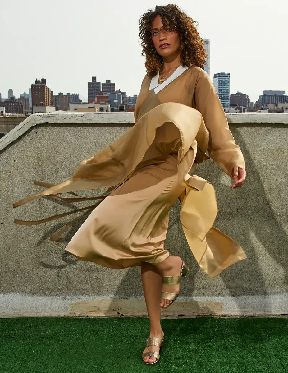 Fashion test shoot, full-length, model Ireland T in a gold satin wrap dress with tie belt in motion, Manhattan skyline, East Village rooftop, New York City, styling by Matsine Stinson, makeup by Stefani Paige Vivian, photographed by Scott Parker Phot
