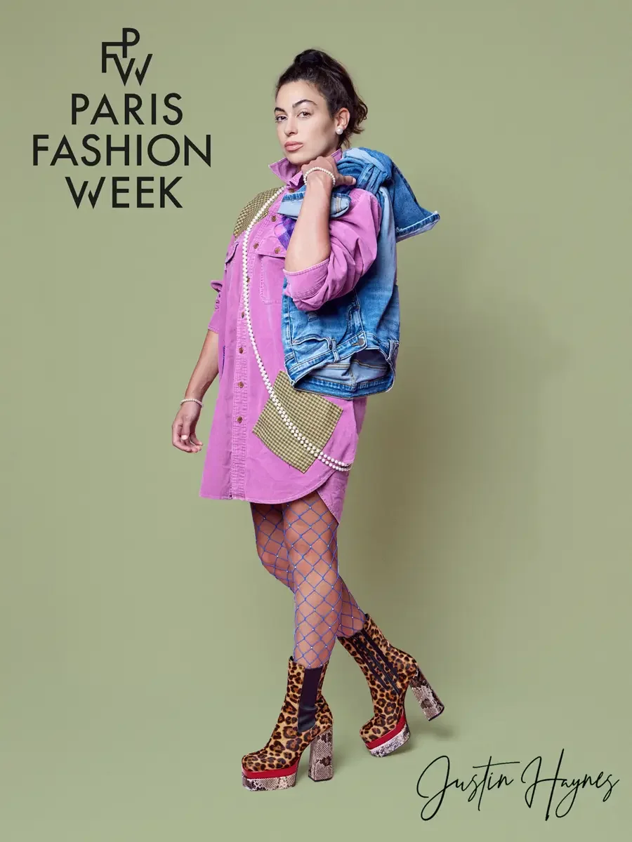 JUS10H 2025 promotional image, model in three-quarter profile, fuchsia oversized patchwork denim shirtdress with olive houndstooth panels, long pearl rope necklace, blue rhinestone fishnet tights and mixed leopard print and snakeskin platform boots, 