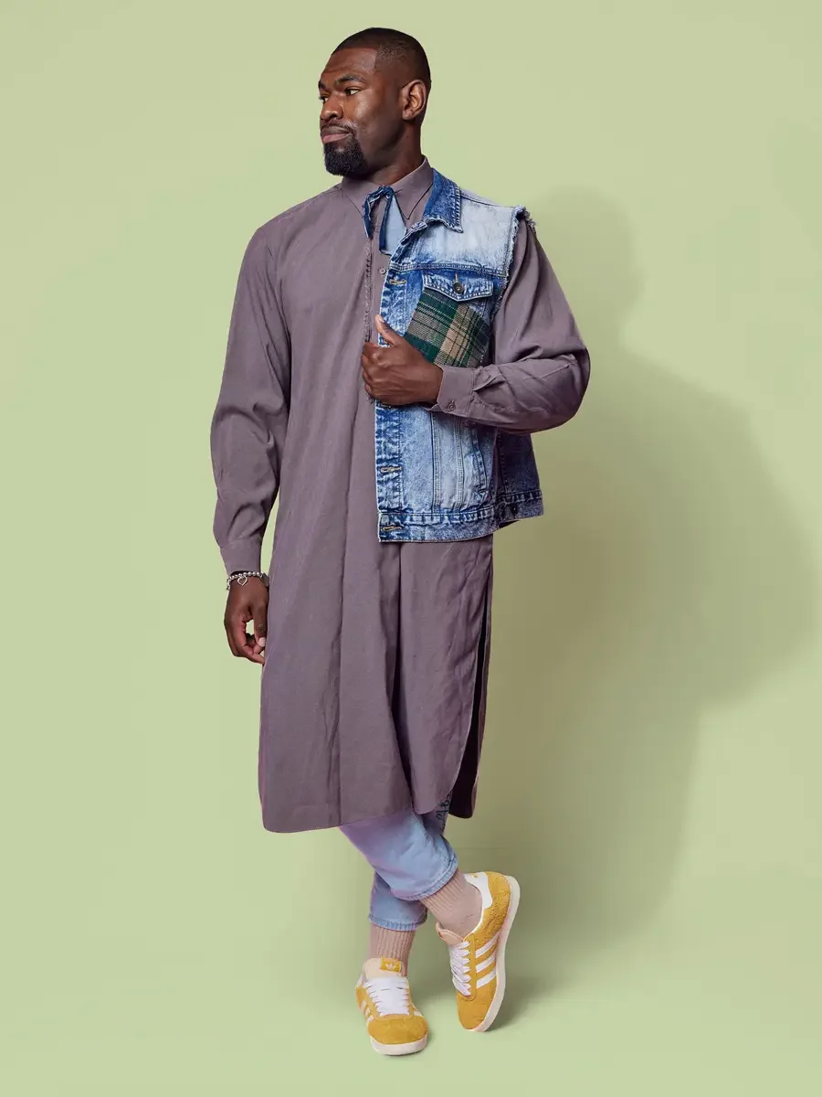 JUS10H 2025 content library, model in three-quarter profile in mauve longline shirt-dress with patchwork denim vest over light blue trousers and yellow sneakers, sage green background, photographed by Scott Parker Photo