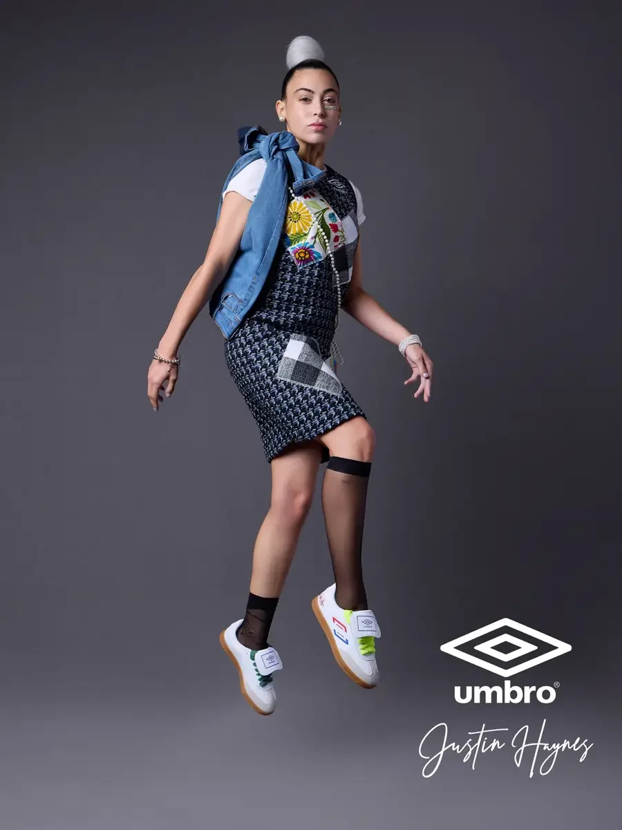 Fashion photographer producer and creative director work for the Umbro France collection. Vanessa mid-leap with one knee raised holding a denim jacket at her collar in a navy houndstooth sleeveless shift dress with diagonal floral and patchwork panel