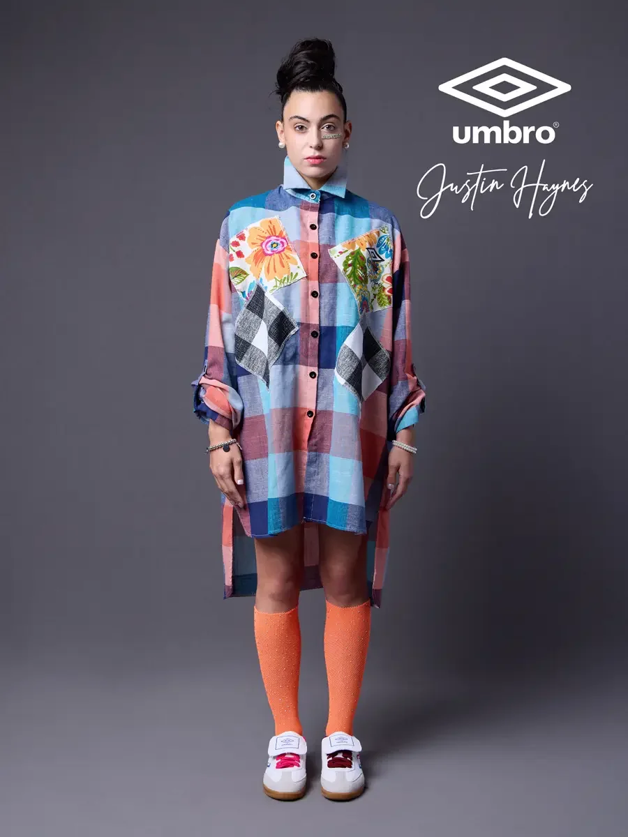 Polished pitch-side style for the Umbro France collection. Vanessa standing front-facing in an oversized multicolor plaid shirt dress with floral patchwork panels and orange football knee socks, styled by Justin Haynes, photographed in Springfield, M