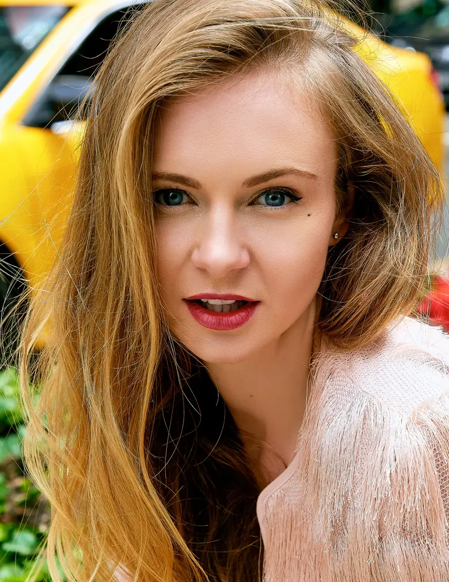 Julia, close-up portrait, blush pink feather-fringe cropped jacket, NYC yellow taxi and street planter with red flowers visible in background, Upper East Side street test shoot, photographed by Scott Parker Photo
