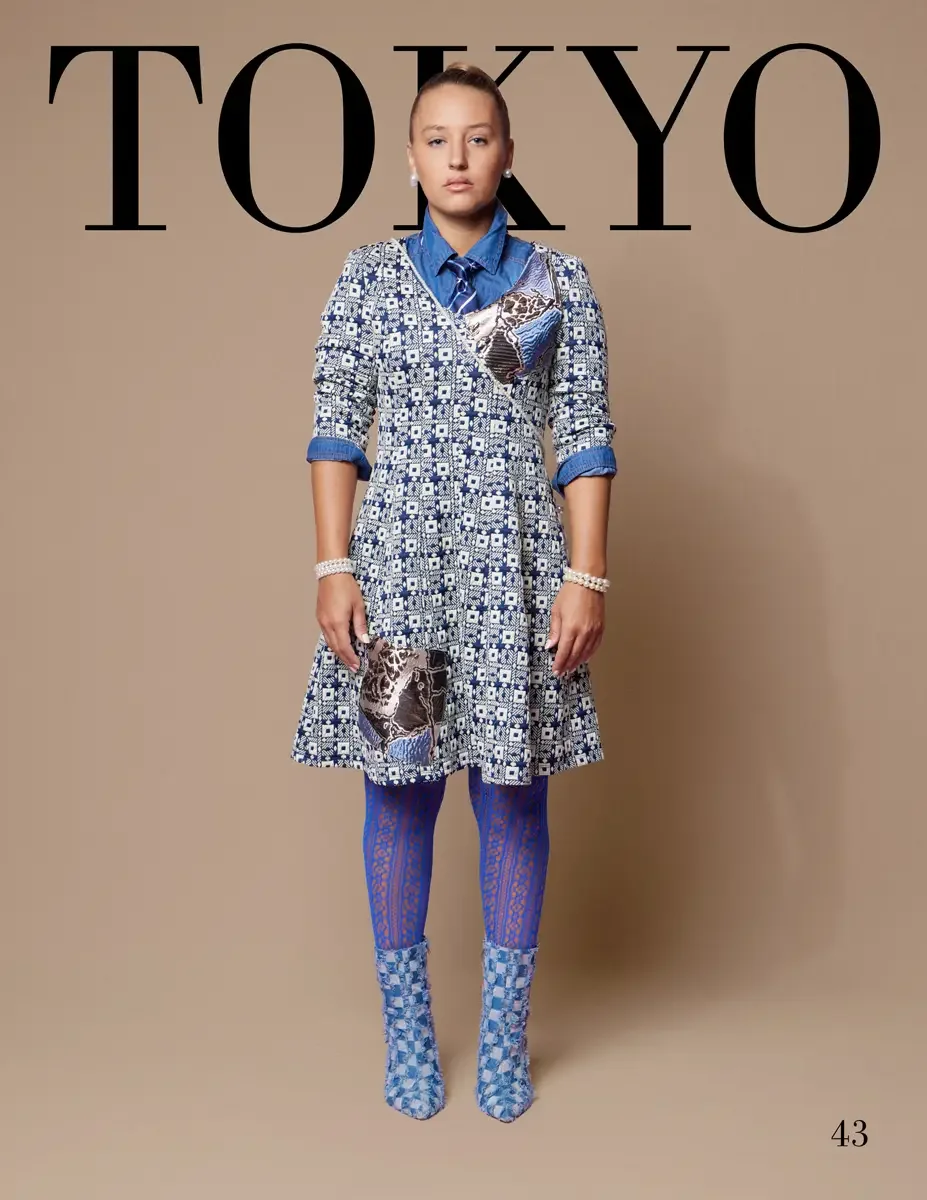 JUS10H 2025 Tokyo lookbook, a female model wearing a blue and white geometric print fit-and-flare dress with metallic snake-print patchwork appliqués, layered over a denim button-down shirt with a denim tie, styled with pearl bracelets, blue lace tig