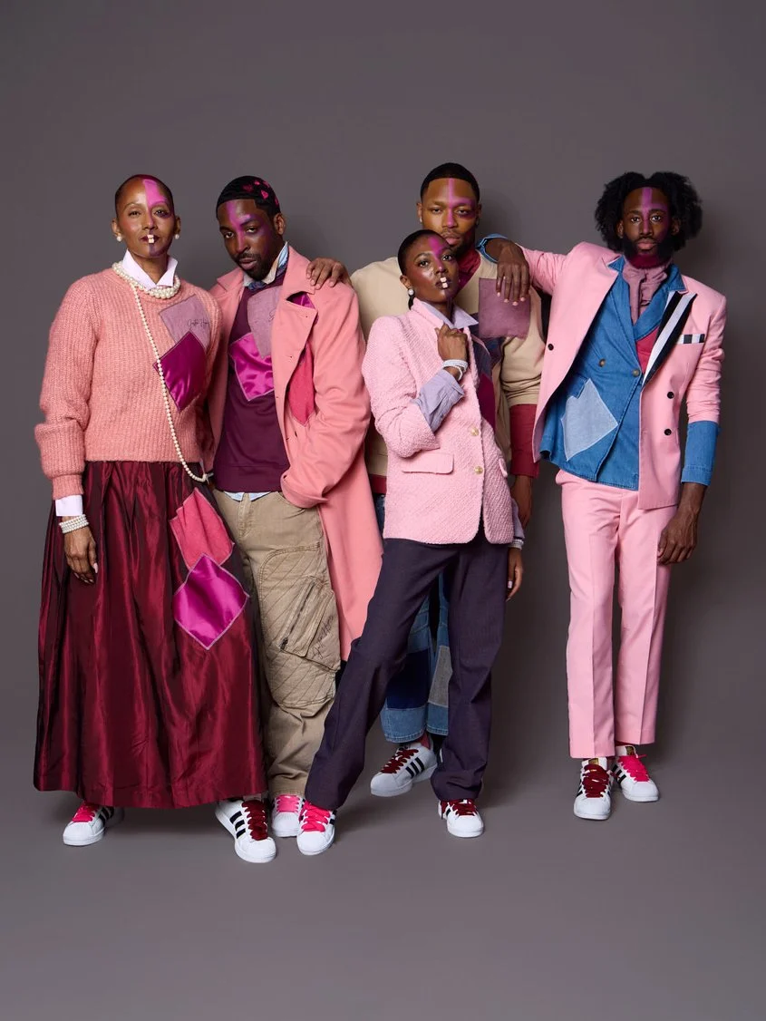 Group of five fashionably dressed people posing together in colorful, coordinated outfits against a gray background.