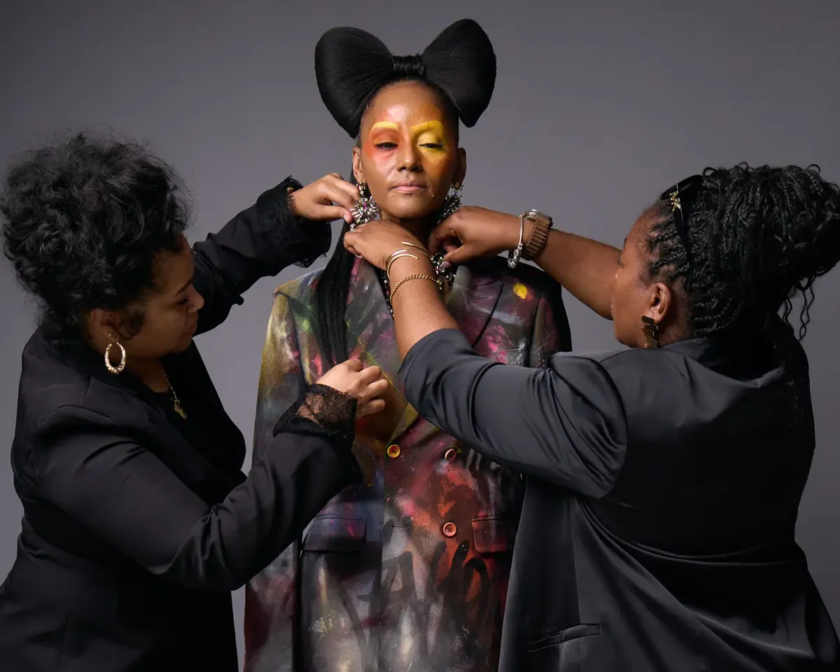 JUS10H Met Monday 2026, beauty and hair team placing jewellry on model on set, hand-painted suit, grey background, photographed by Scott Parker Photo