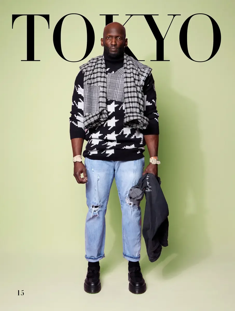 JUS10H 2025 Tokyo lookbook, oversized houndstooth knit sweater with glen plaid vest draped over shoulders and distressed light wash jeans, spring green background, photographed by Scott Parker Photo for the Tokyo Fashion Council