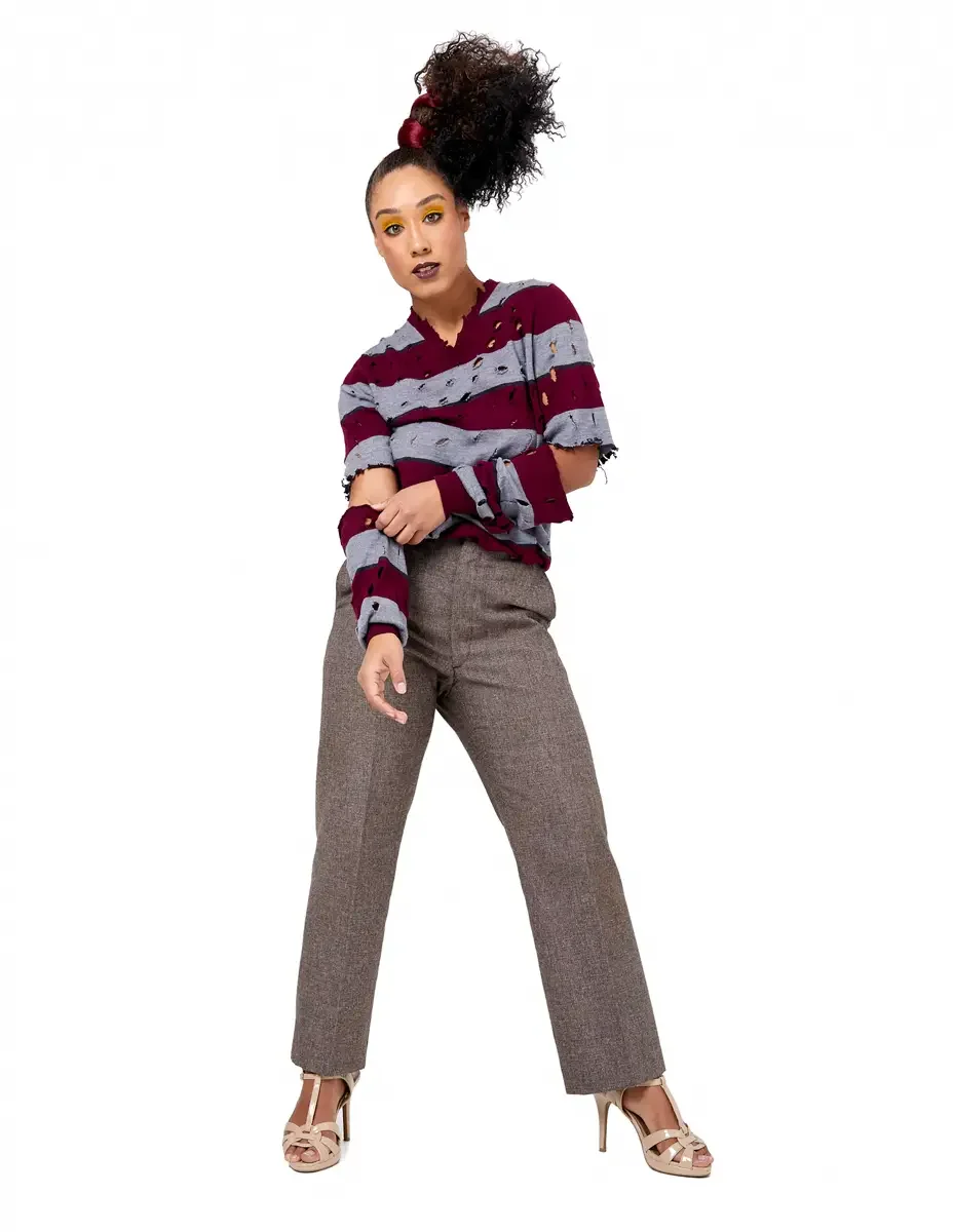 Model portfolio development session, high fashion editorial look, burgundy and heather grey destroyed-knit stripe sweater with raw-edge cutout sleeves, straight-leg heathered trousers, nude t-strap heels, blazer removed, full-length, relaxed stance, 