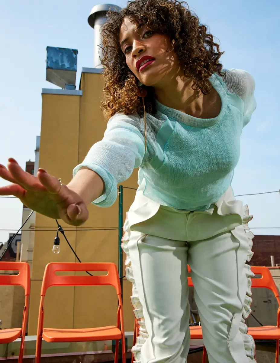 Fashion test shoot, model Ireland T in Amy Page DeBlasio white ruffle-trim pants with front zipper and aqua sheer knit top, East Village rooftop, New York City, styling by Matsine Stinson, makeup by Stefani Paige Vivian, photographed by Scott Parker 