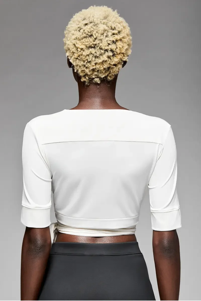 Minika Ko lookbook, white wrap crop top, back view, clean back panel with horizontal seam at shoulder, wrap ties crossing at waist, elbow-length sleeves, photographed by Scott Parker Photo