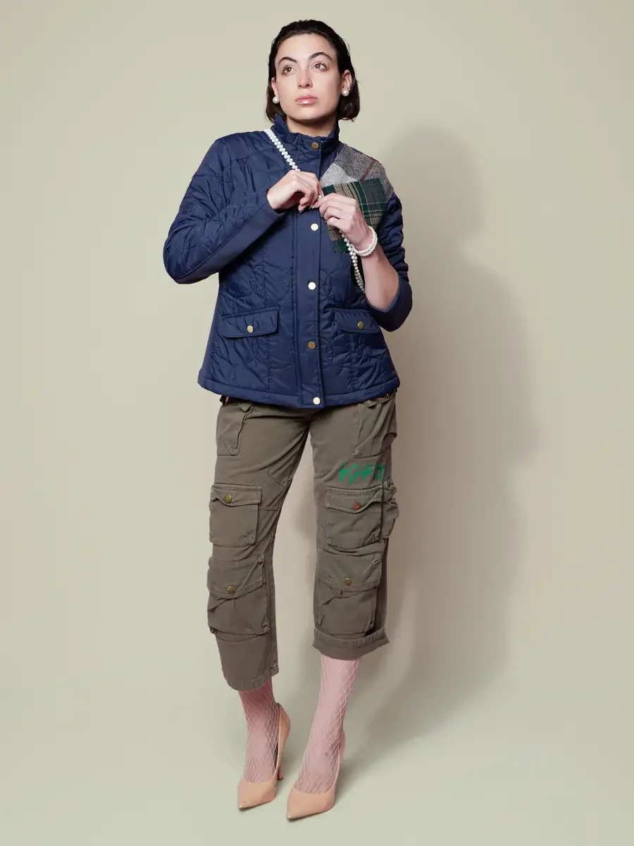 JUS10H 2025 Billboard Magazine UAE feature, model in navy quilted patchwork jacket with tartan and herringbone shoulder panel, pearl necklace, and olive multi-pocket cargo trousers, sage background, photographed by Scott Parker Photo