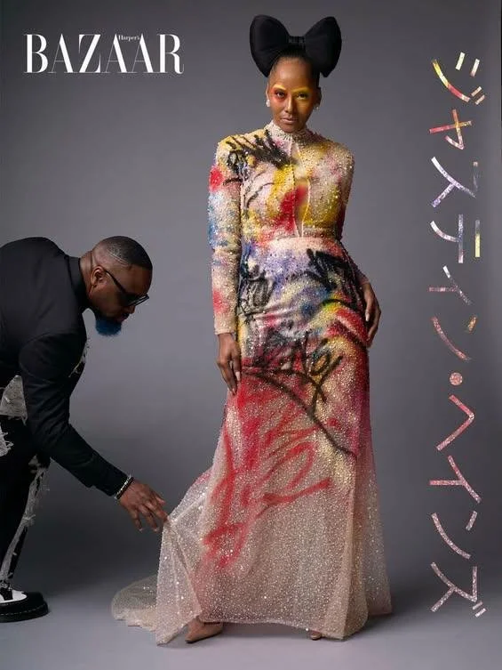 A woman modeling a colorful, graffiti-style designed gown with a large black bow headpiece, standing next to a person holding the train of her dress, against a plain gray background with 'Harper's BAZAAR' logo and Japanese text. Met Monday. Met Gala.