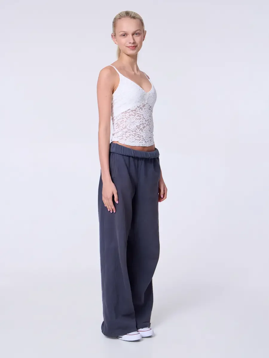 Model portfolio development session, commercial look, white lace crop camisole top and wide-leg charcoal sweatpants with elastic waistband, full-length, three-quarter turn, arms at sides, soft smile, wide leg of sweatpant showing full drape, white Co