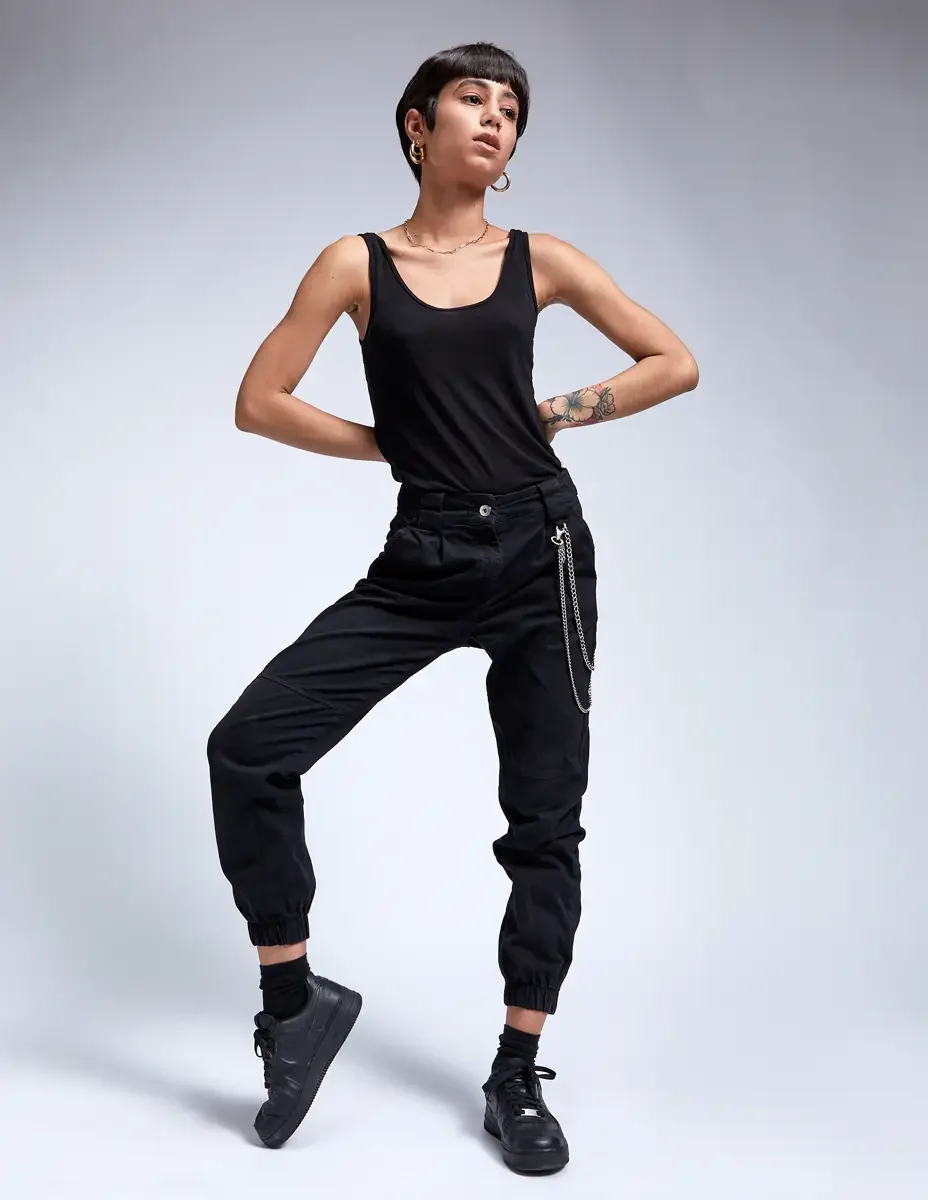 Eloissa, dynamic stance, black tank and black cargo jogger pants with chain detail, floral forearm tattoo, East Williamsburg studio test shoot, makeup by Schanica Pickens, photographed by Scott Parker Photo