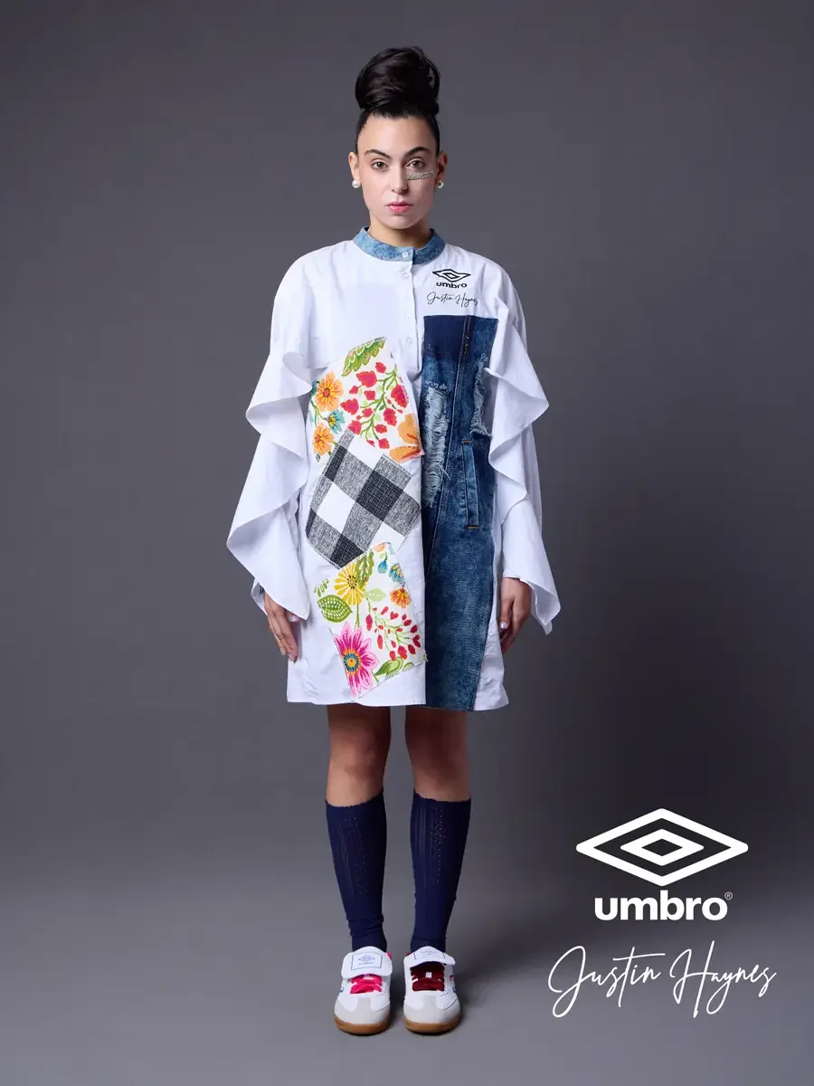 Editorial fashion photography for the Umbro France collection. Vanessa standing front-facing in an oversized white shirt dress with dramatic ruffled sleeves, a distressed denim center panel, and floral patchwork, styled by Justin Haynes, photographed