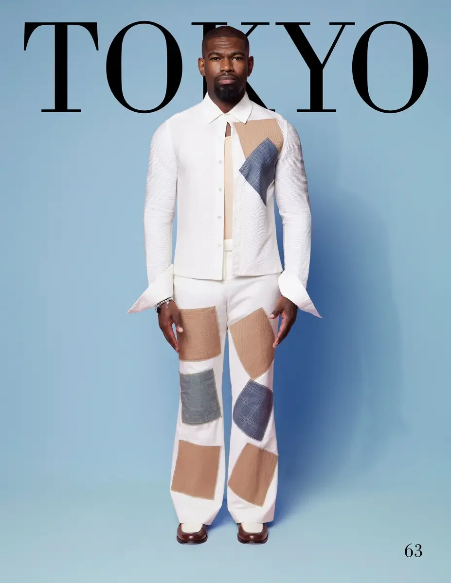 JUS10H 2025 Tokyo lookbook, a male model wearing a white textured knit button-front jacket with tan, gray, and blue patchwork appliqués, a cream knit tie, and wide-leg white trousers with large tan, gray, and blue patchwork panels, a chain bracelet, 