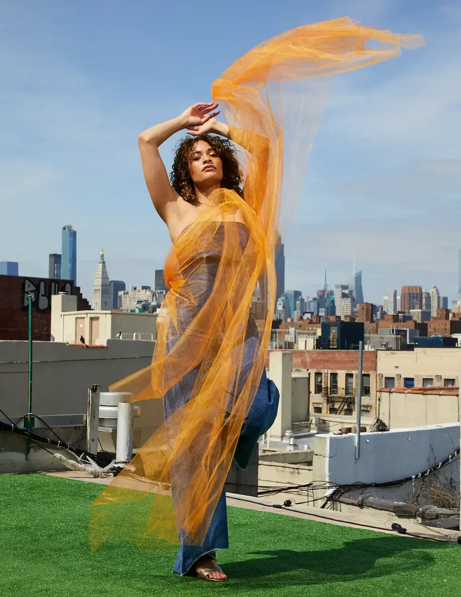 Fashion test shoot, model Ireland T in Amy Page DeBlasio wide-leg textured blue pants and navy strapless top, orange tulle wrapping figure, East Village rooftop, New York City, styling by Matsine Stinson, makeup by Stefani Paige Vivian, photographed 