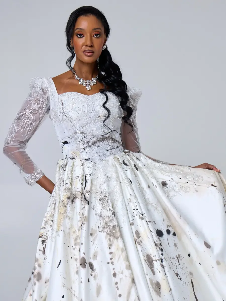 JUS10H 2025 New York Bridal Fashion Week, white abstract paint-splatter ball gown with beaded sweetheart bodice, sheer embroidered puff sleeves, and crystal waist belt, styled with a crystal cluster necklace and drop earrings, photographed by Scott P