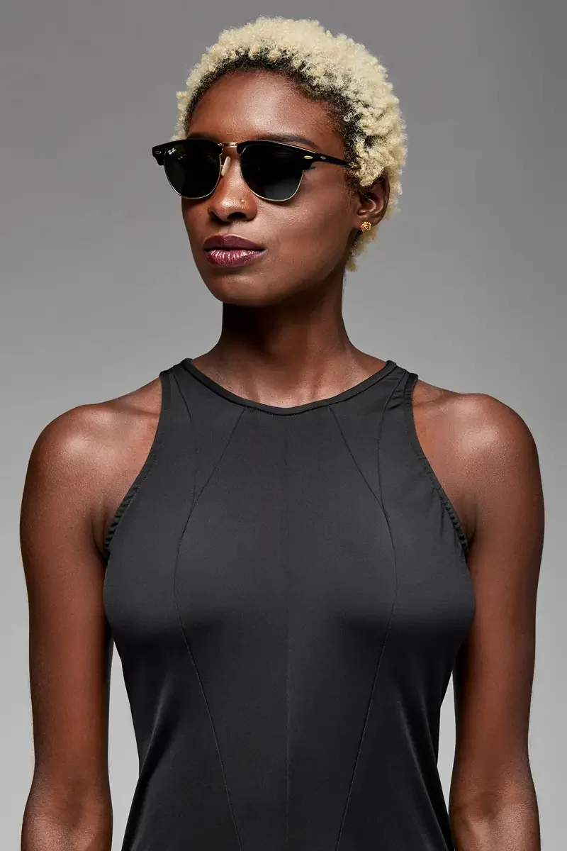 Minika Ko lookbook, detail, black sleeveless jumpsuit, close crop showing high halter neckline, angled seam at shoulder, and upper bodice construction, dark sunglasses, photographed by Scott Parker Photo